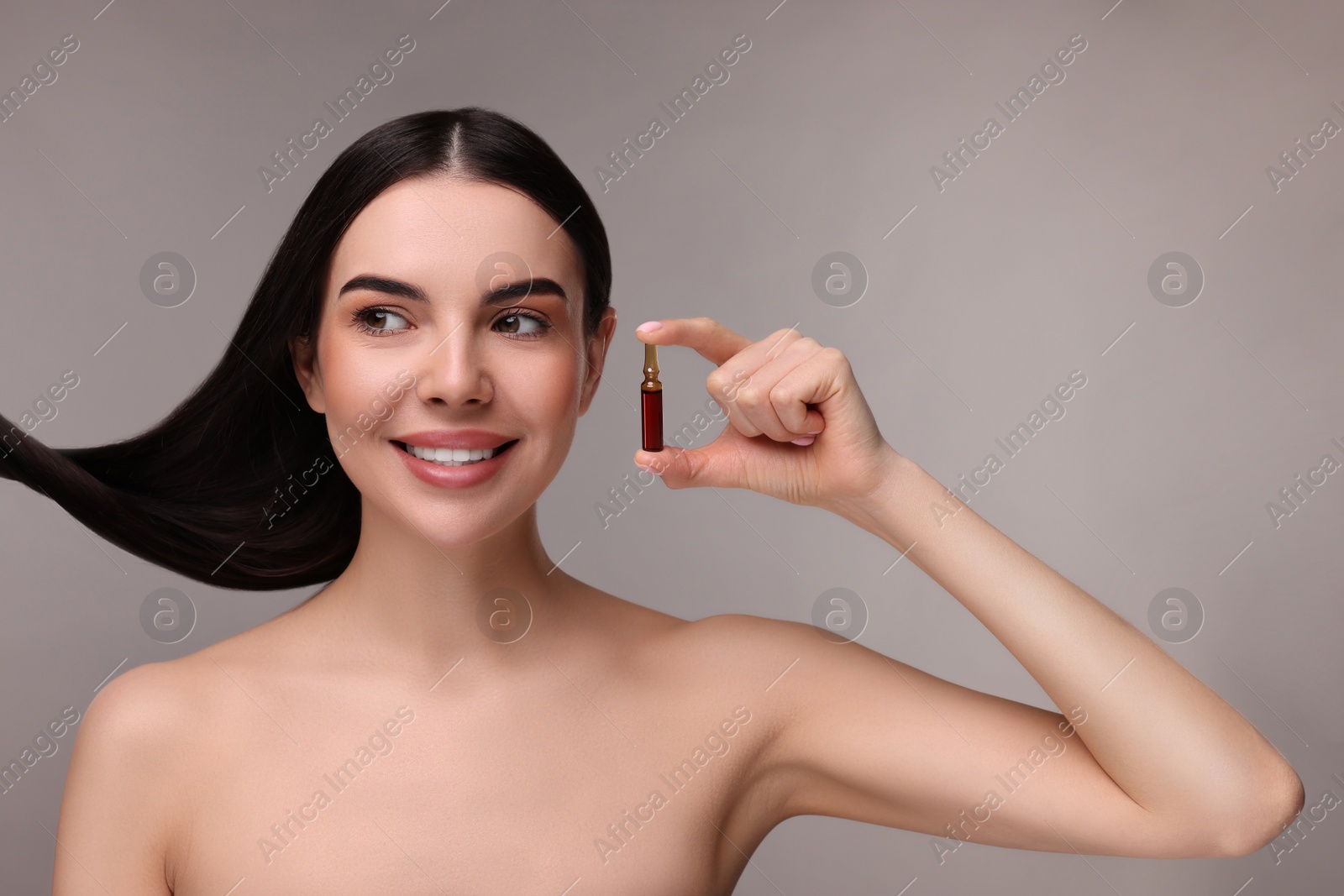 Photo of Beautiful young woman with long healthy hair holding ampoule on grey background