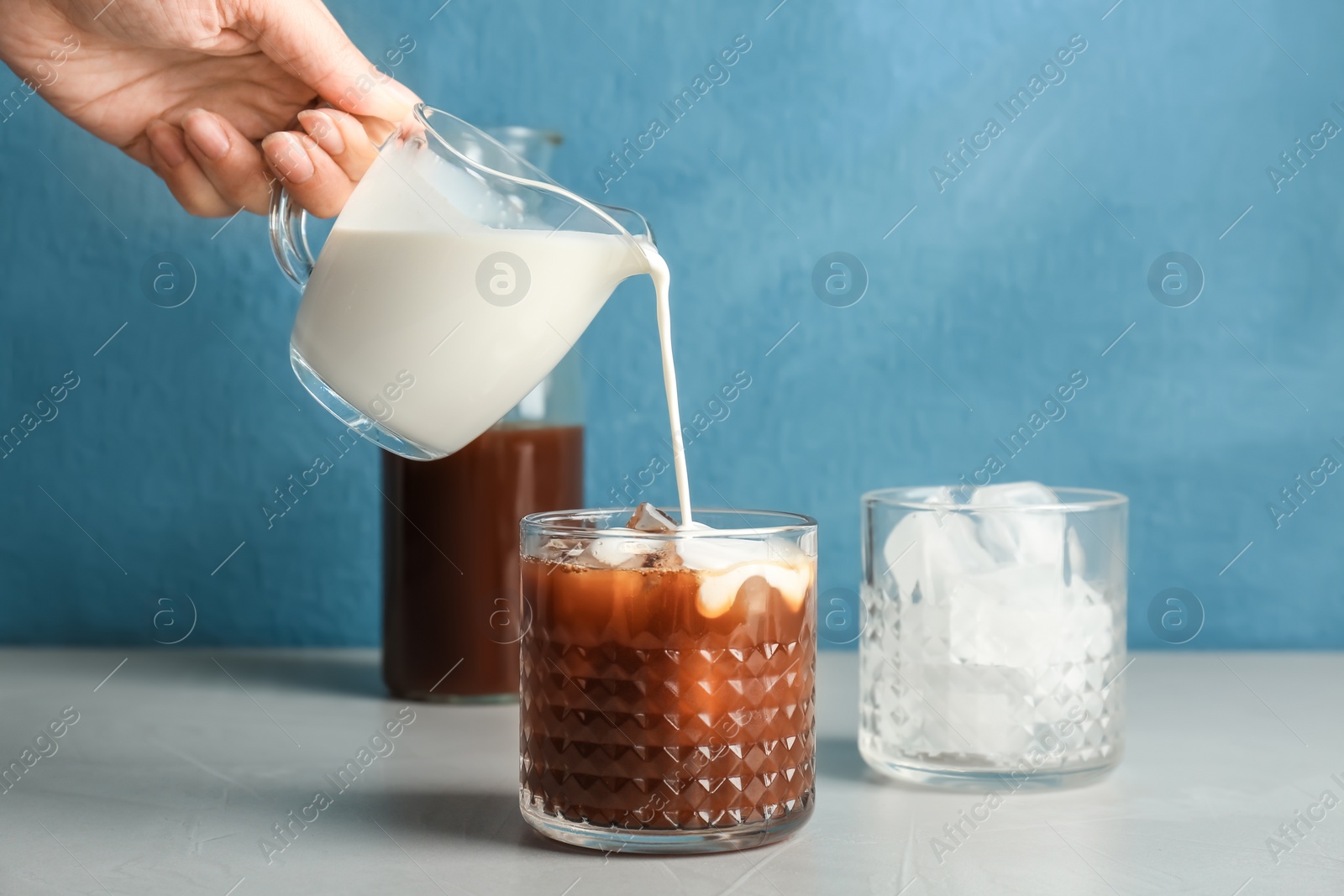 Photo of Woman pouring milk into glass with cold brew coffee on table