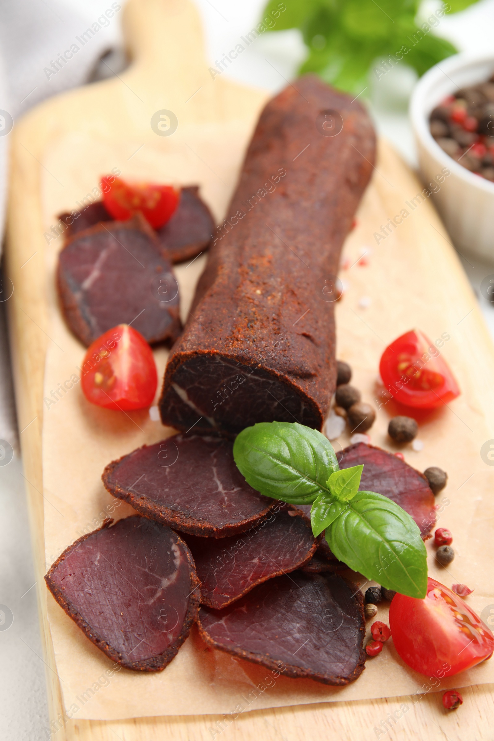 Photo of Delicious dry-cured beef basturma with basil and tomatoes on table, closeup