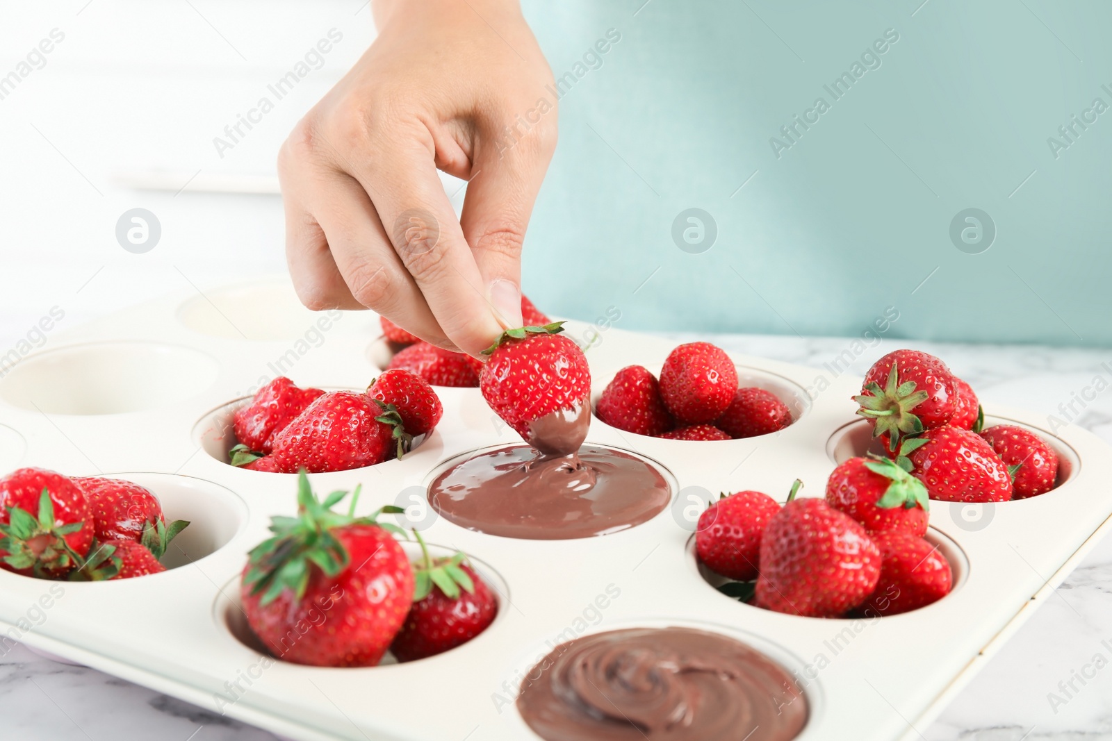 Photo of Woman dipping ripe strawberry into mold with melted chocolate, closeup