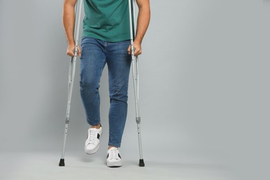 Photo of Young man with axillary crutches on grey background, closeup. Space for text