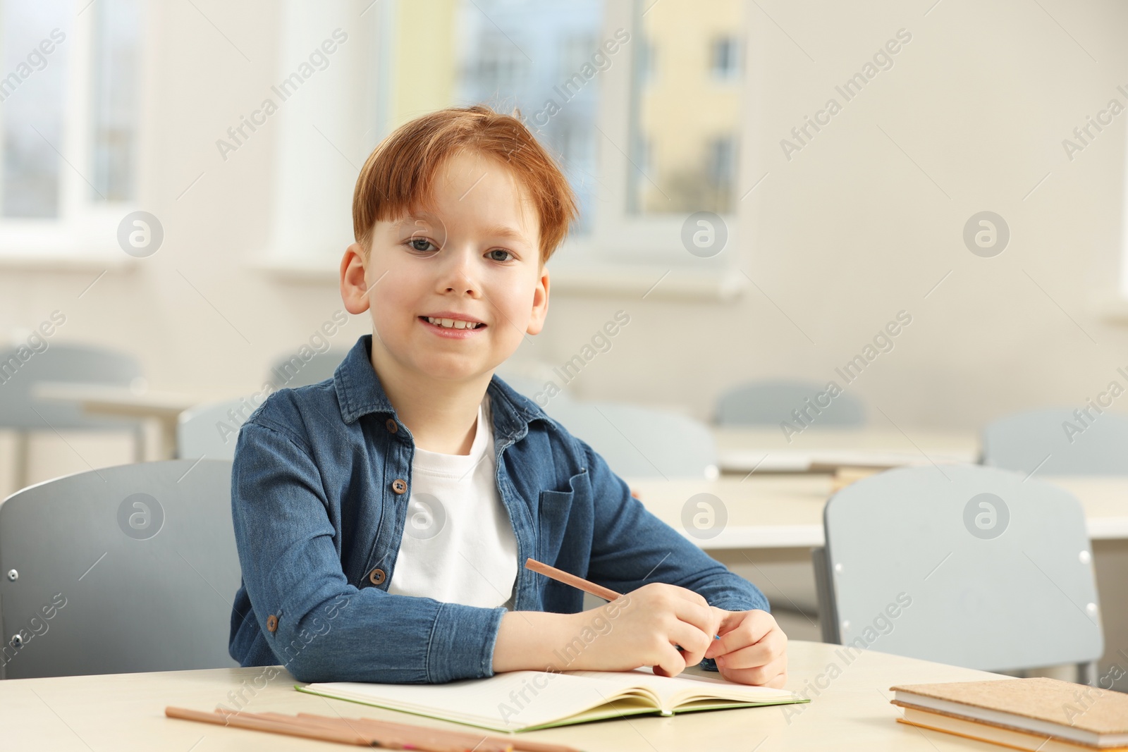 Photo of Portrait of smiling little boy studying in classroom at school. Space for text