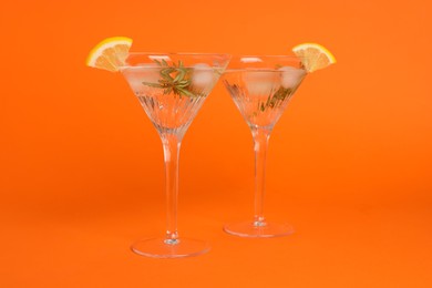 Photo of Martini glasses of refreshing cocktail with lemon slices and rosemary on orange background