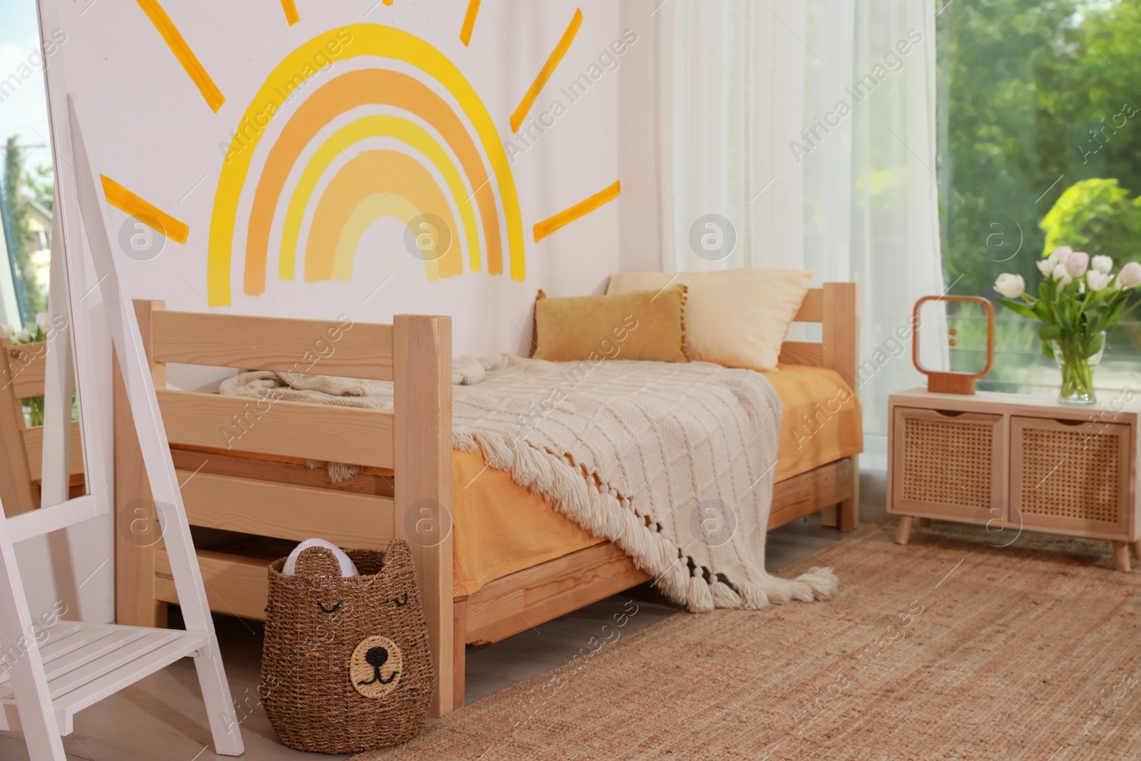 Photo of Cute child's room interior with bed and sun art on wall