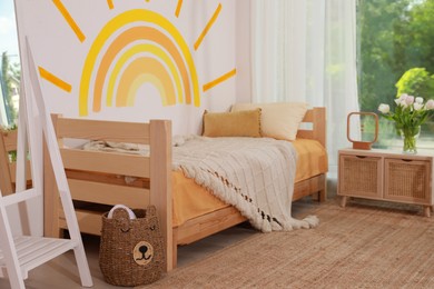 Photo of Cute child's room interior with bed and sun art on wall