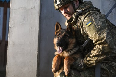 Photo of Ukrainian soldier with German shepherd dog outdoors. Space for text