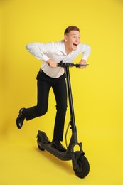 Emotional man riding modern electric kick scooter on yellow background