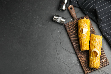 Delicious boiled corn served on black table, flat lay. Space for text