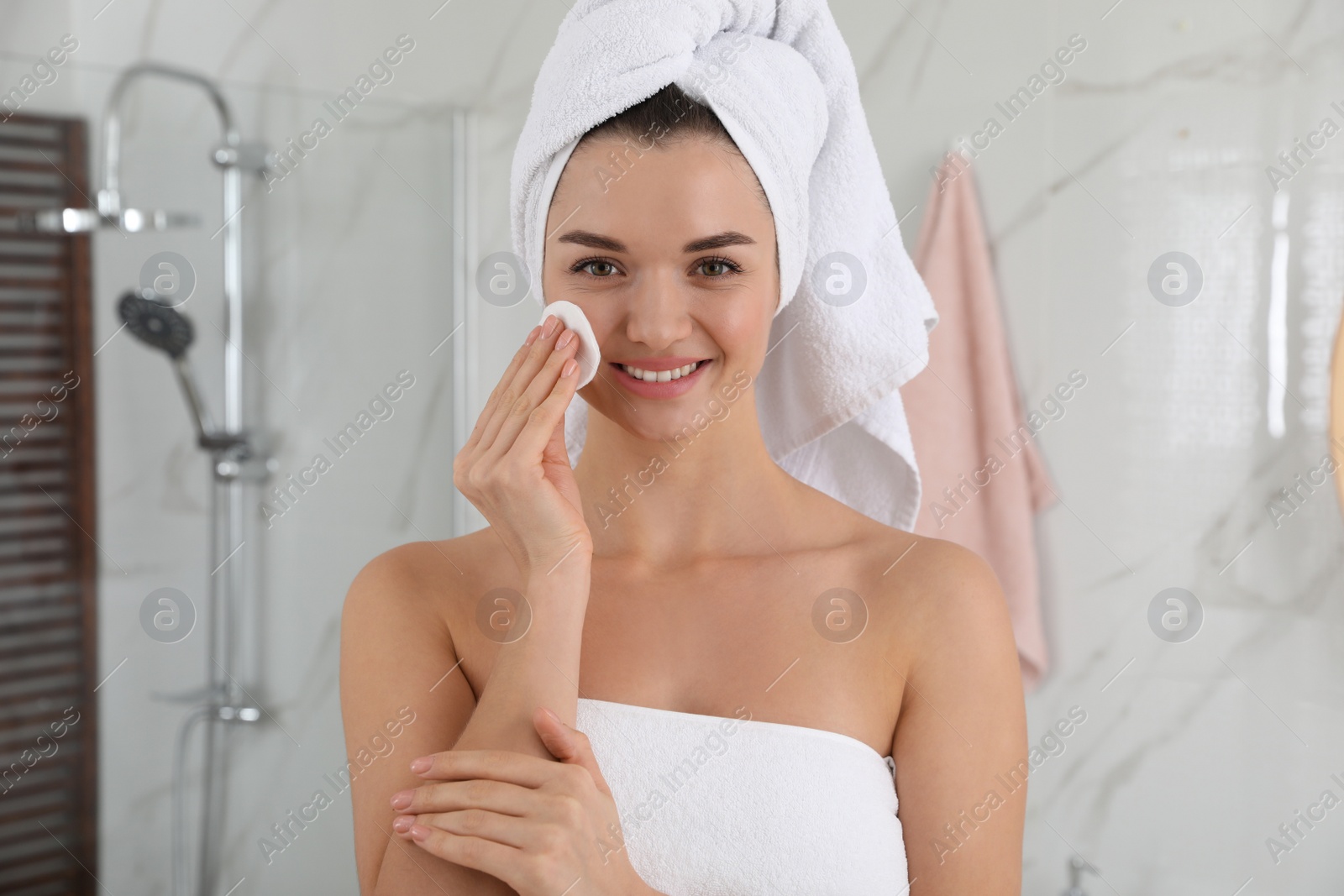 Photo of Beautiful young woman with hair wrapped in towel cleaning her face indoors