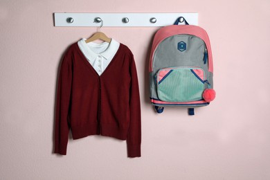 Photo of Shirt, backpack and jumper hanging on pink wall. School uniform