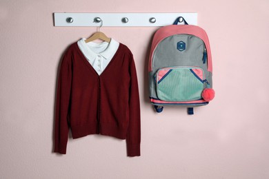 Shirt, backpack and jumper hanging on pink wall. School uniform