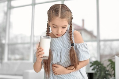 Photo of Little girl with dairy allergy holding glass of milk indoors