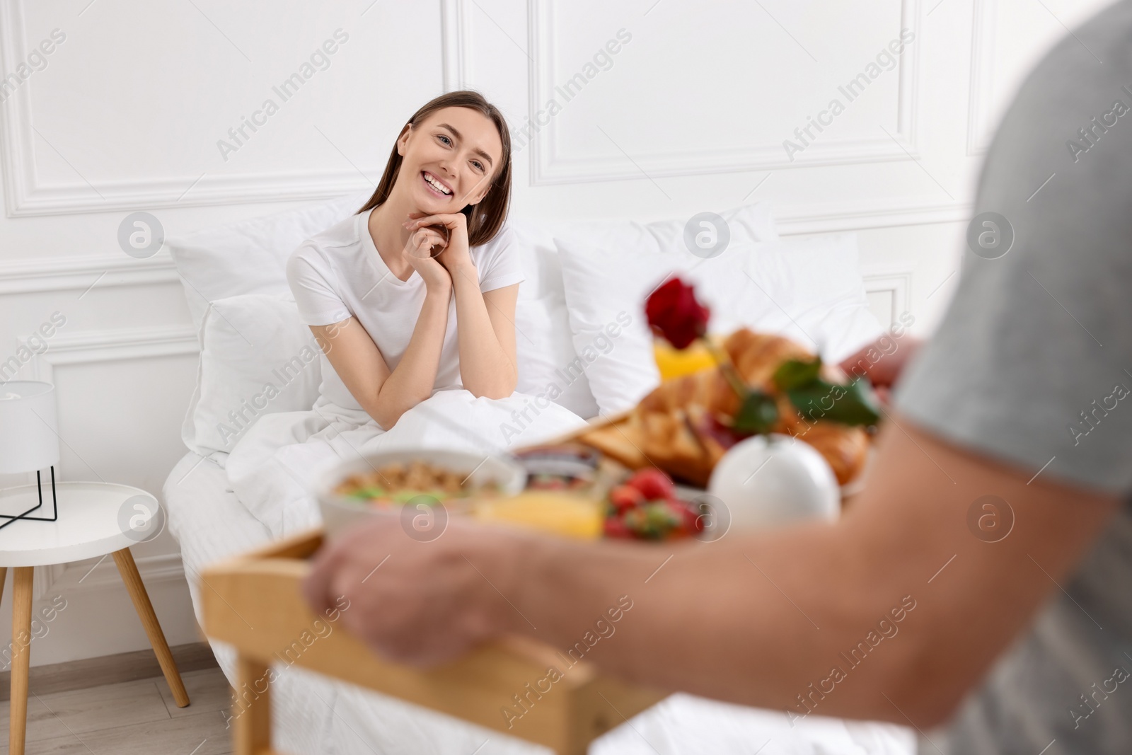 Photo of Romantic breakfast. Husband bringing tray with tasty food to his happy wife in bedroom, closeup