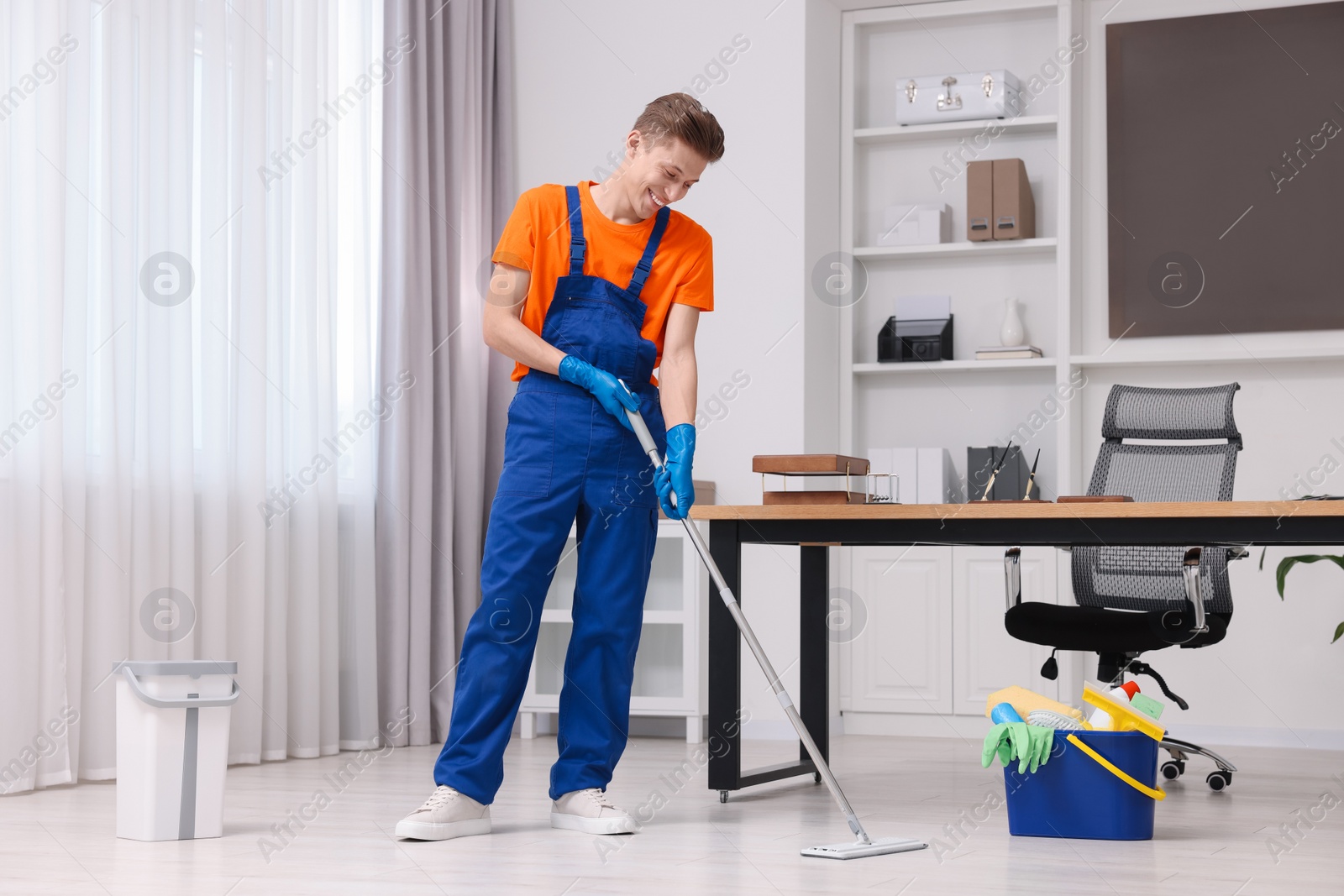 Photo of Cleaning service worker washing floor with mop. Bucket with supplies in office