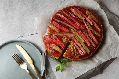 Freshly baked rhubarb pie and cutlery on light grey table, flat lay