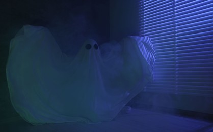 Creepy ghost. Woman covered with sheet near window in blue light