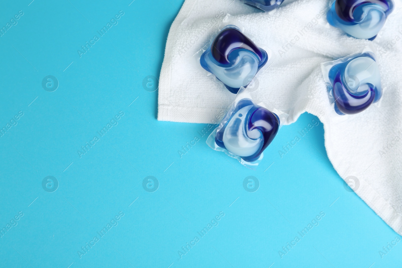 Photo of Laundry capsules and towel on light blue background, flat lay. Space for text