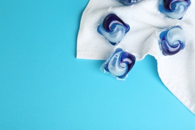 Laundry capsules and towel on light blue background, flat lay. Space for text