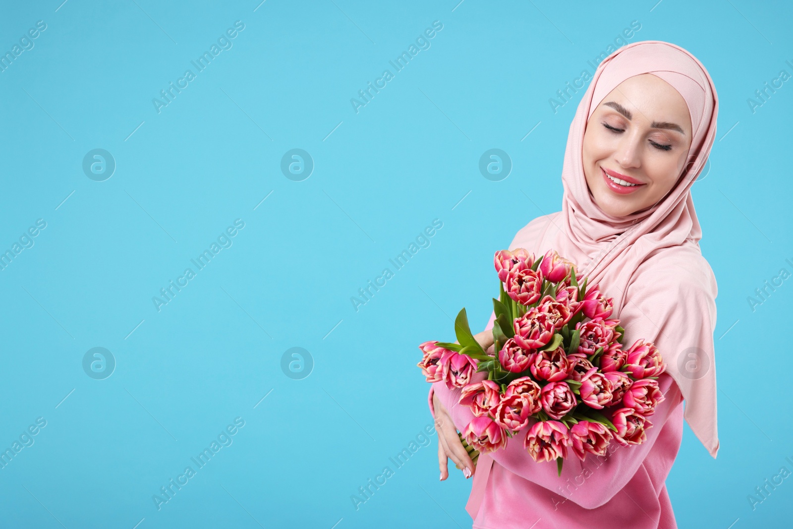 Photo of Happy woman in hijab with beautiful bouquet on light blue background. Space for text