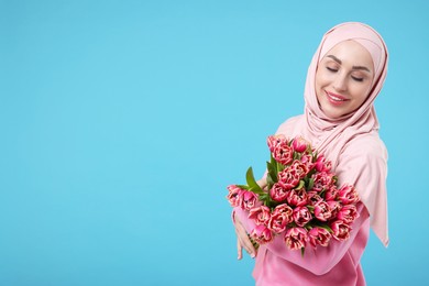 Photo of Happy woman in hijab with beautiful bouquet on light blue background. Space for text