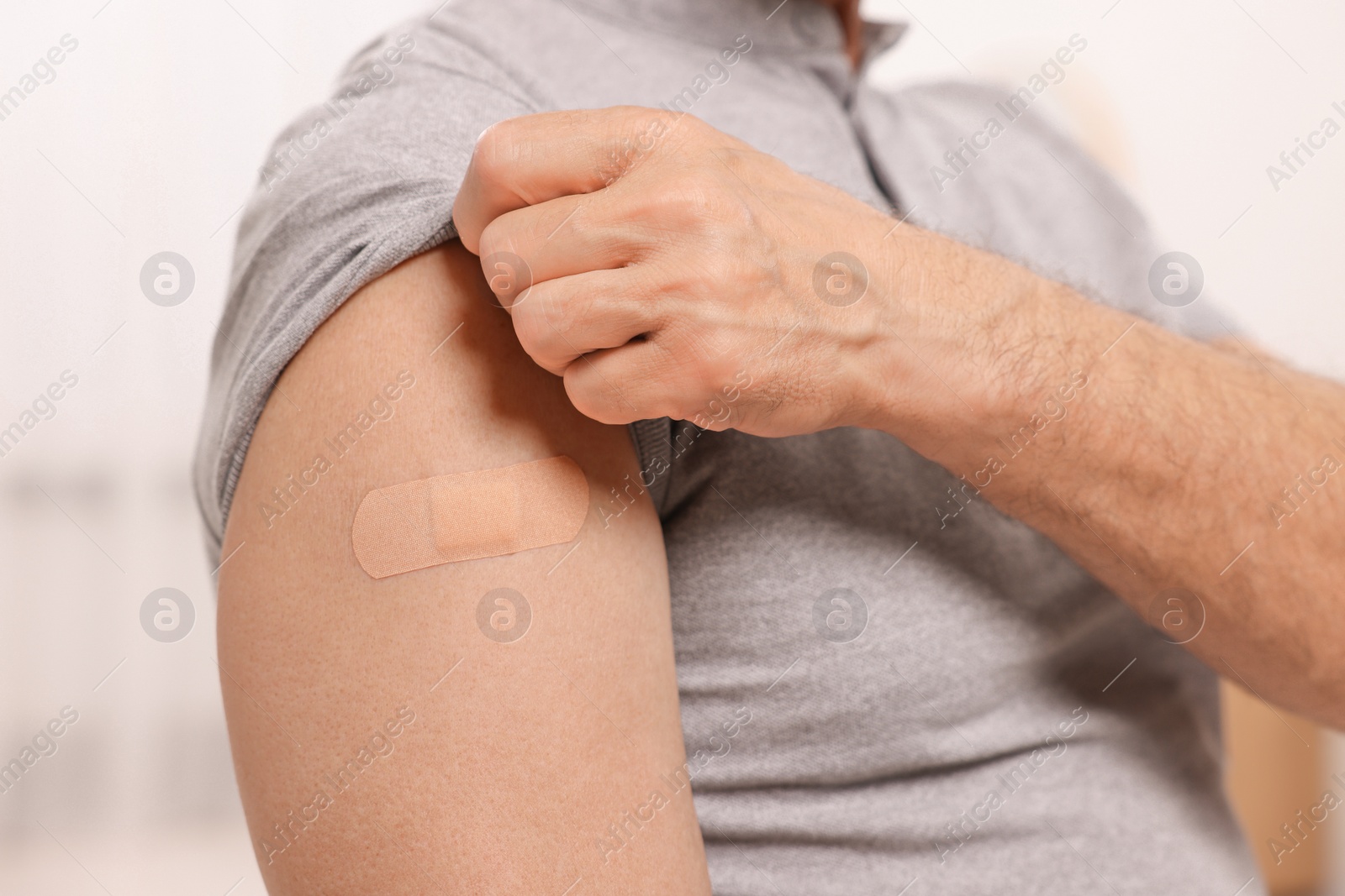 Photo of Man with adhesive bandage on his arm after vaccination against blurred background, closeup