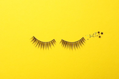 Photo of False eyelashes and sparkles on yellow background, flat lay