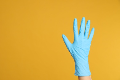 Photo of Doctor wearing medical gloves on yellow background, closeup. Space for text