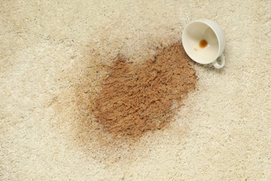 Photo of Overturned cup and spilled coffee on beige carpet, top view