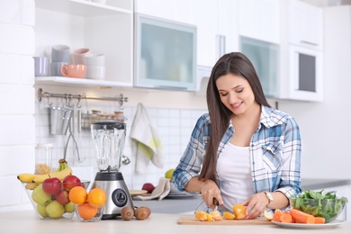 Photo of Young woman preparing tasty healthy smoothie at table in kitchen