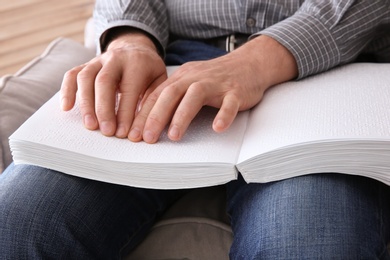 Photo of Blind man reading book written in Braille at home, closeup
