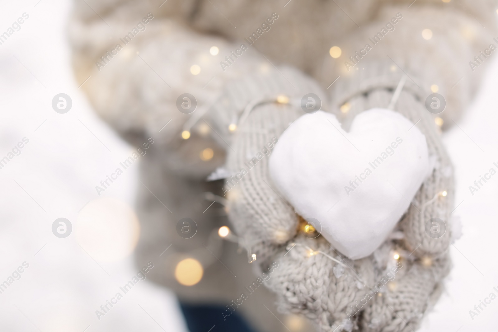 Photo of Woman holding Christmas lights and heart made of snow, closeup
