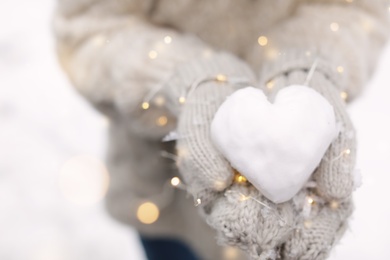 Woman holding Christmas lights and heart made of snow, closeup