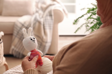 Elderly woman with knitted bunny at home, closeup. Creative hobby