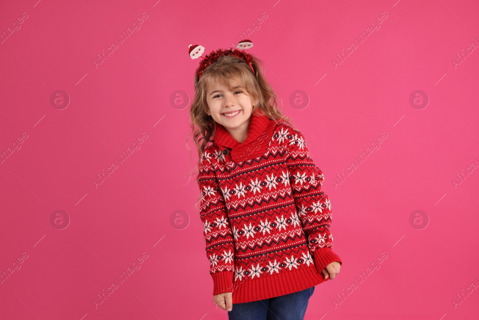 Photo of Cute little girl in red Christmas sweater smiling against pink background