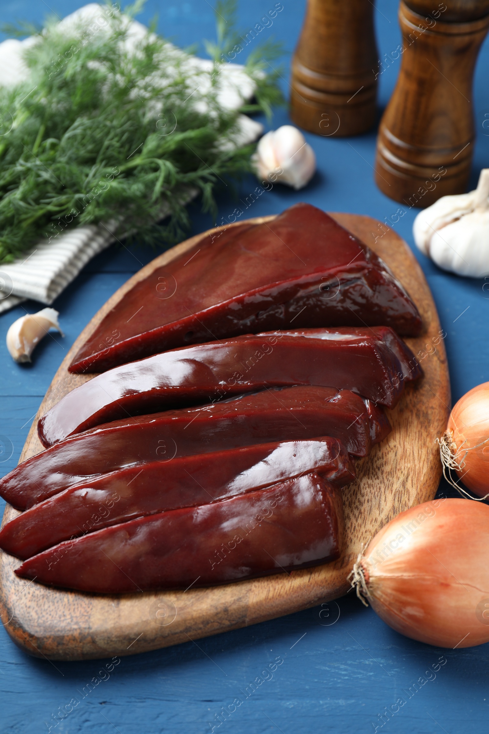 Photo of Cut raw beef liver with onions, garlic, dill and spices on blue wooden table, closeup