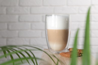 Glass of tasty coffee and caramel candies on wooden table against brick wall, space for text