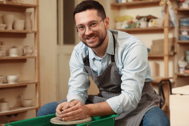 Photo of Happy man crafting with clay on potter's wheel in workshop