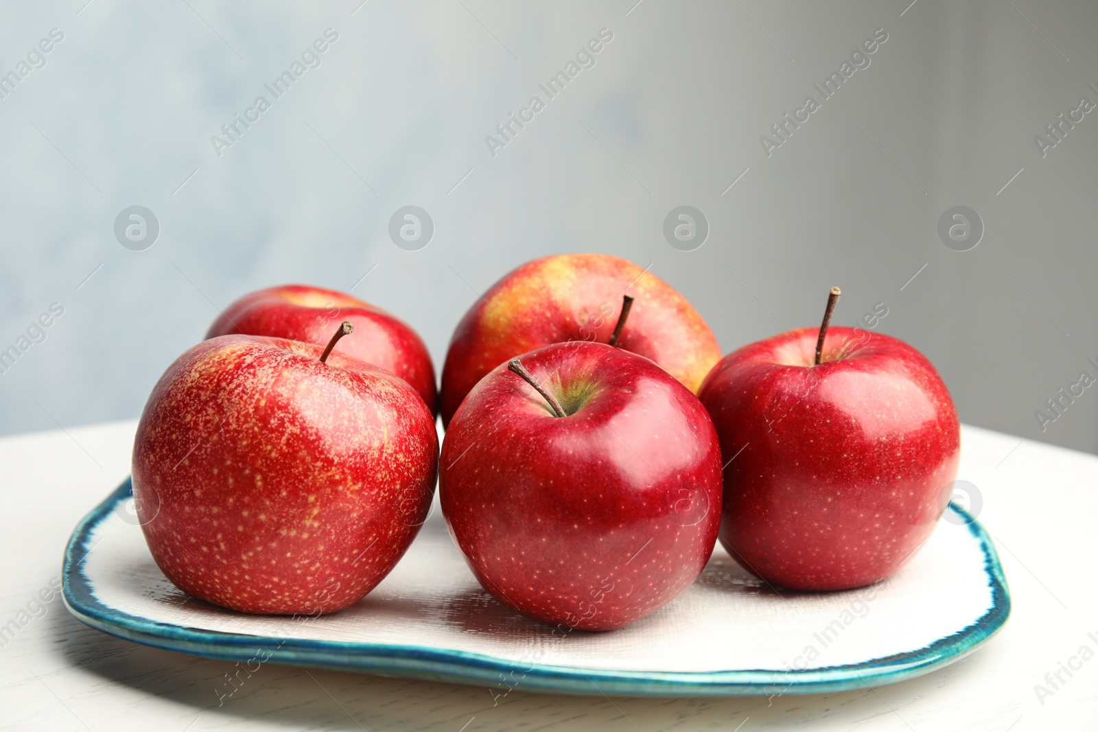 Photo of Plate with ripe juicy red apples on white wooden table against grey background