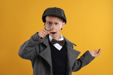 Cute little detective with magnifying glass on yellow background