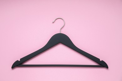 Photo of Empty black hanger on pink background, top view