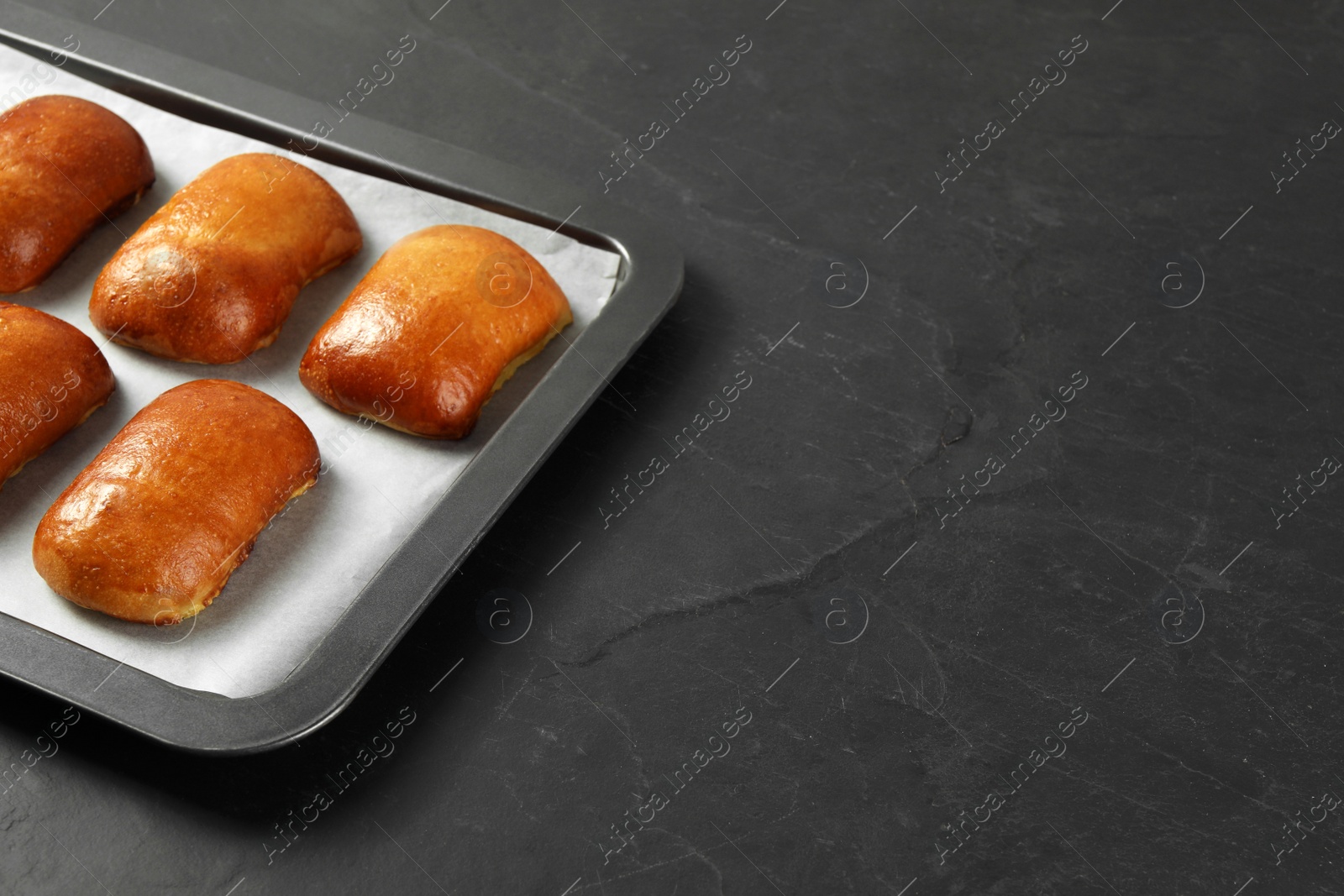 Photo of Delicious baked pirozhki on black table, space for text