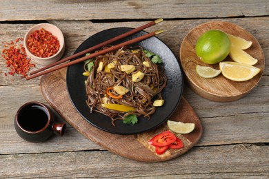 Photo of Stir-fry. Tasty noodles with vegetables and meat served on wooden table, flat lay