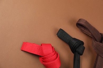 Photo of Colorful karate belts on brown background, flat lay. Space for text