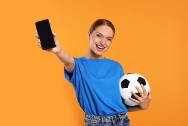 Photo of Happy fan with football ball showing smartphone on orange background