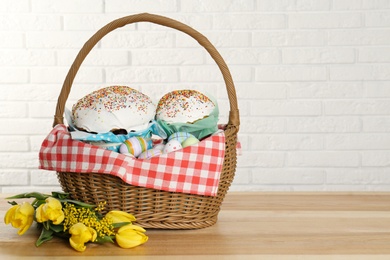 Basket with delicious Easter cakes, dyed eggs and flowers on wooden table. Space for text