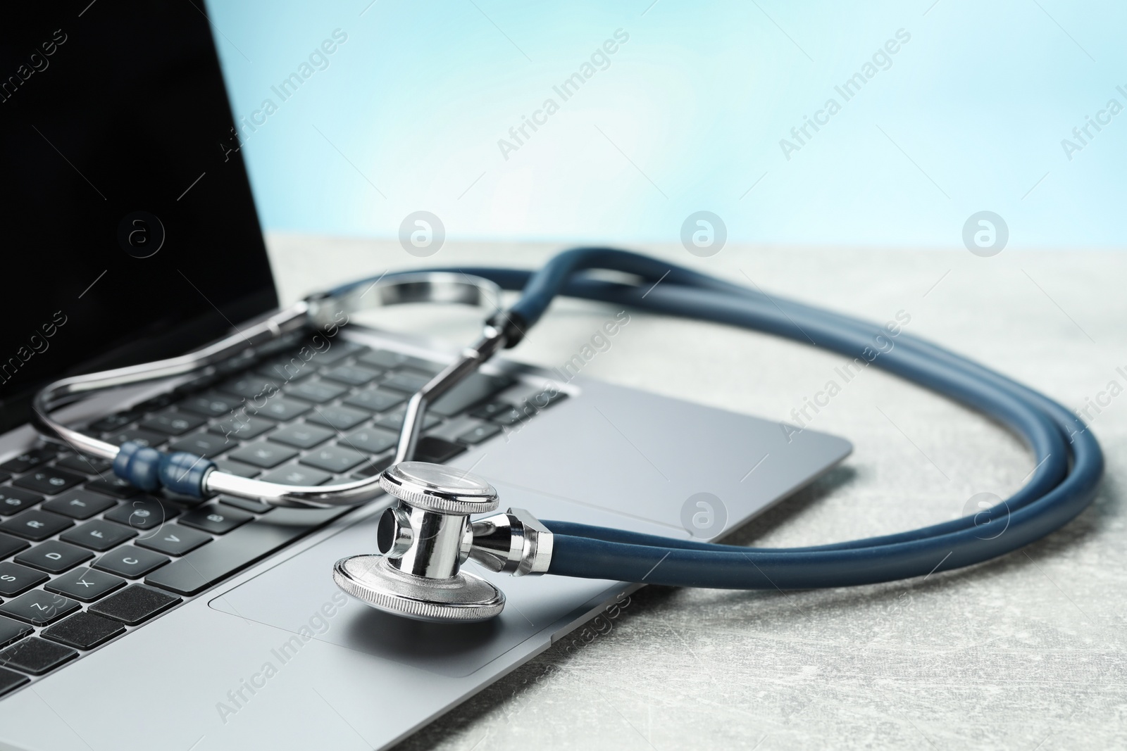 Photo of Stethoscope and modern laptop on grey table, closeup