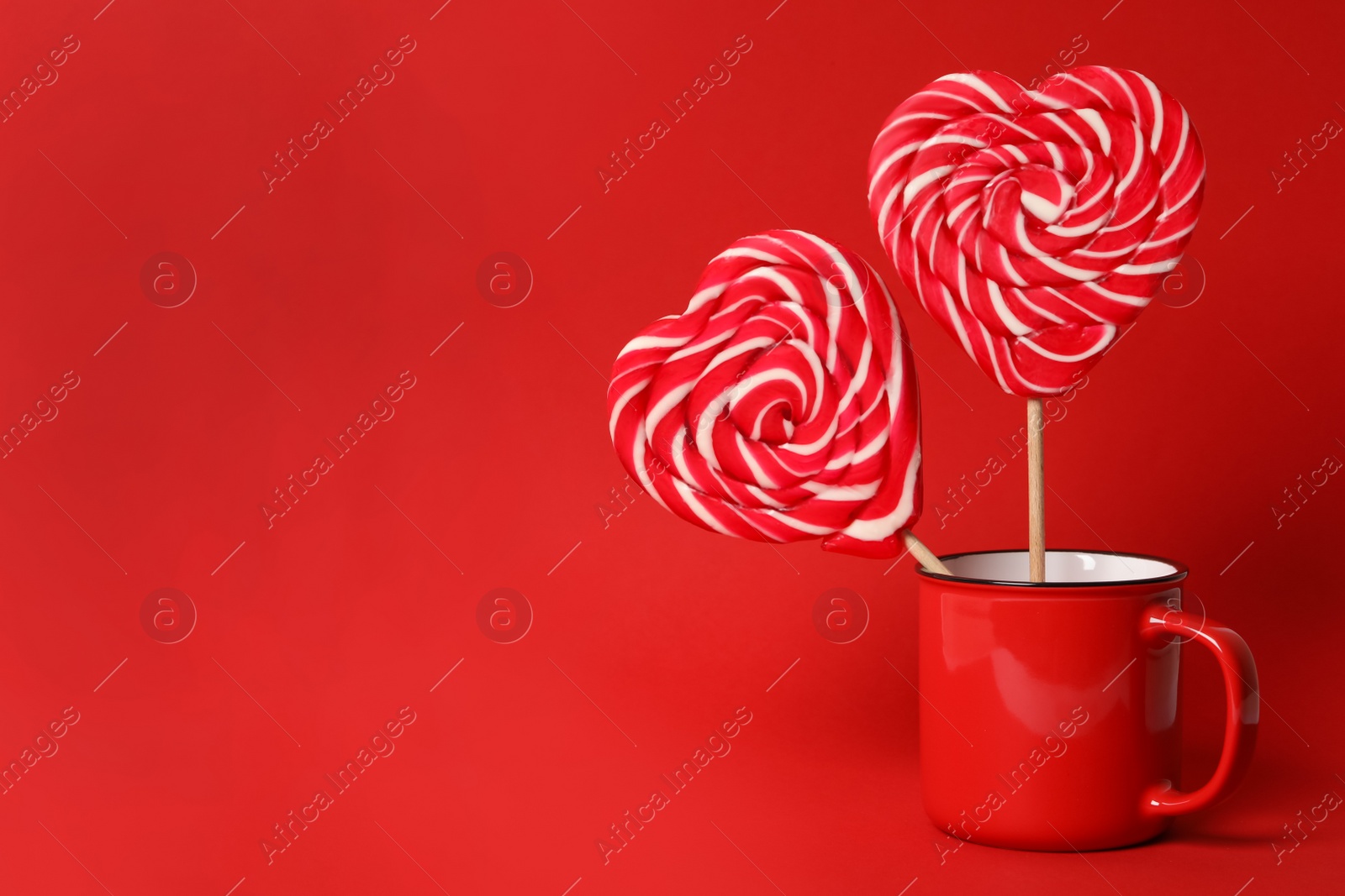 Photo of Sweet heart shaped lollipops in cup on red background, space for text. Valentine's day celebration