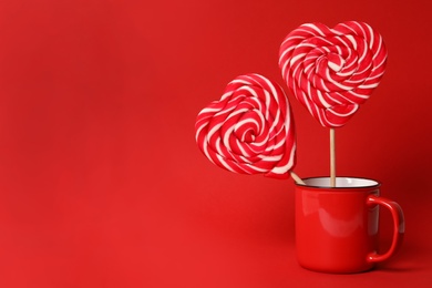 Photo of Sweet heart shaped lollipops in cup on red background, space for text. Valentine's day celebration