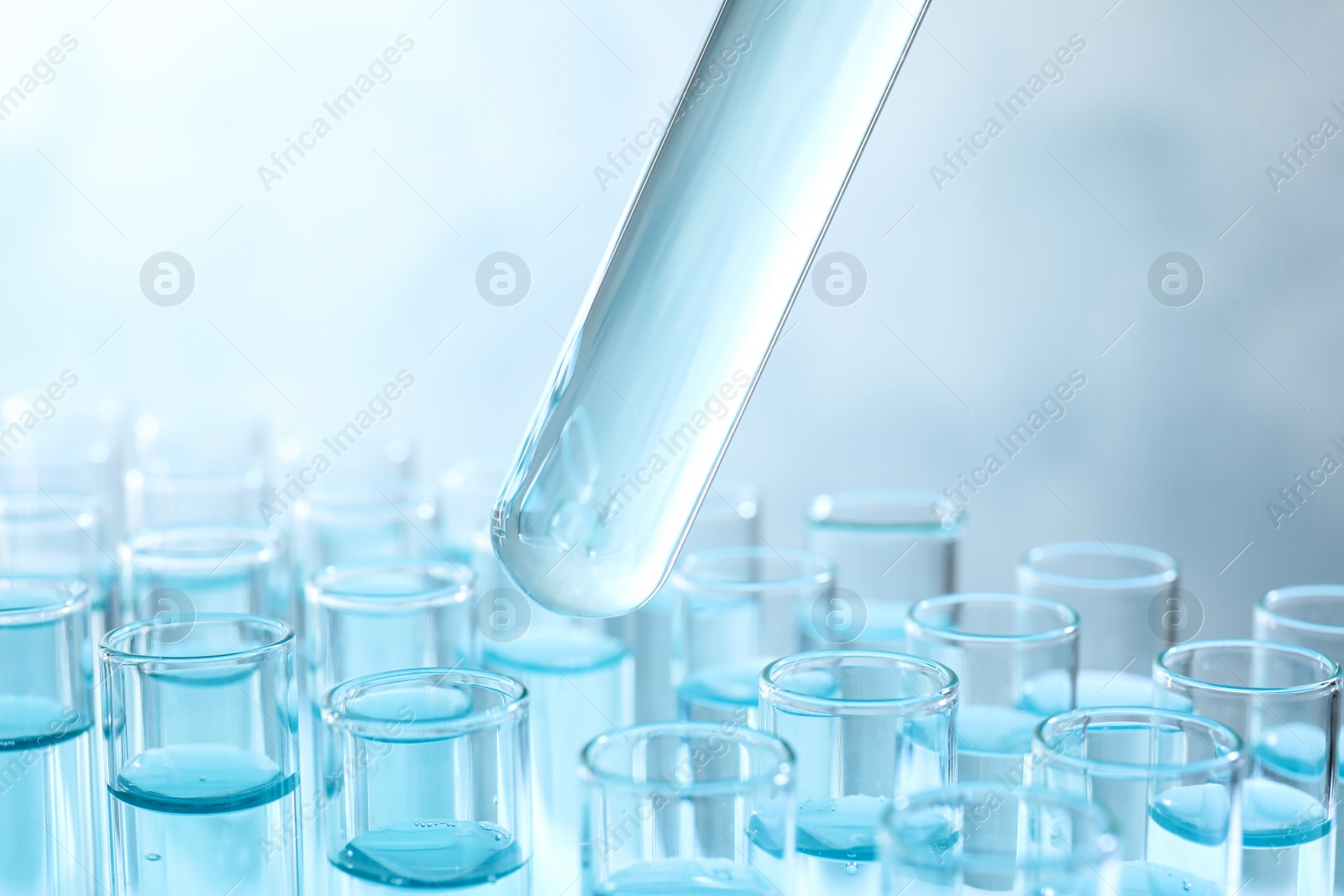 Photo of Taking test tube with liquid sample on light background, closeup