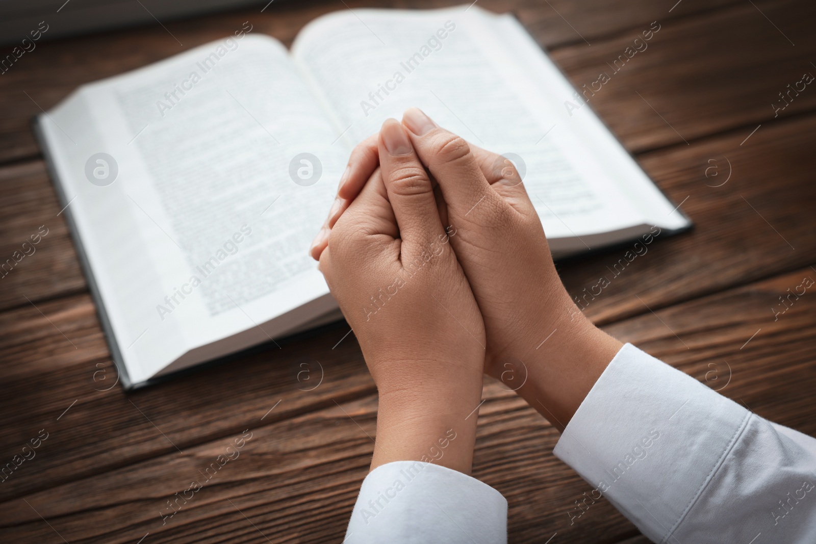 Photo of Woman holding hands clasped while praying at wooden table with Bible, closeup
